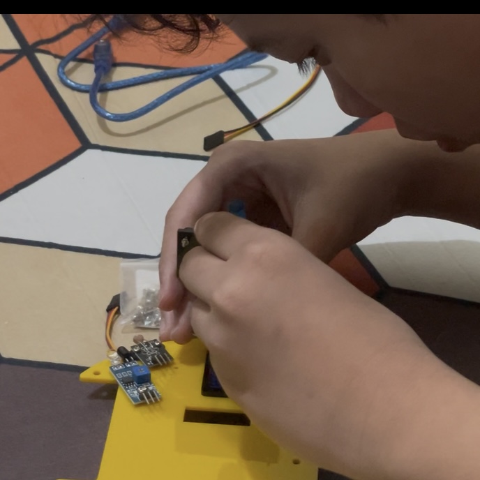 Hands assembling a small yellow wheeled robot